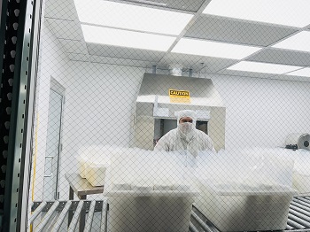 An operator in a face mask, hood, and body coverall prepares pre-wetted wiper orders inside Valutek's cleanroom.